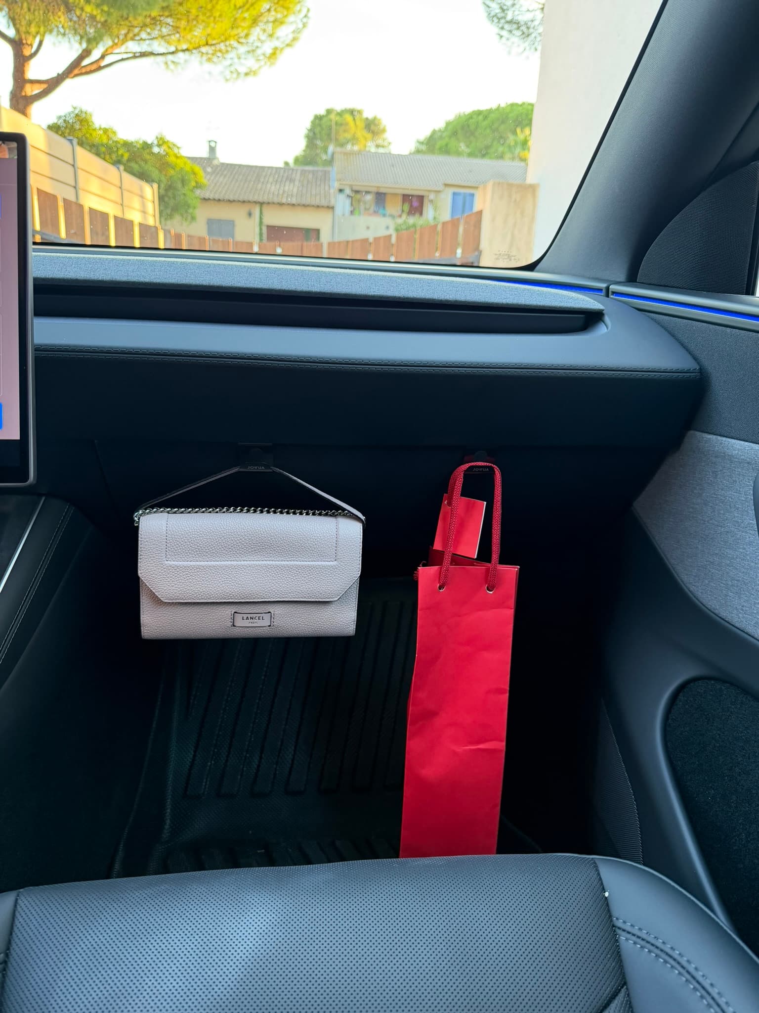 Les deux crochets Jowua sur la boîte à gants de ma Tesla Model Y Juniper, avec un sac à main et une bouteille de vin suspendus